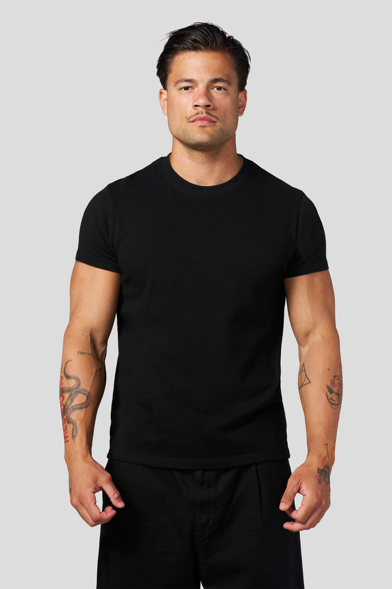 A man modeling a plain black short-sleeve crewneck t-shirt against a solid light gray background.